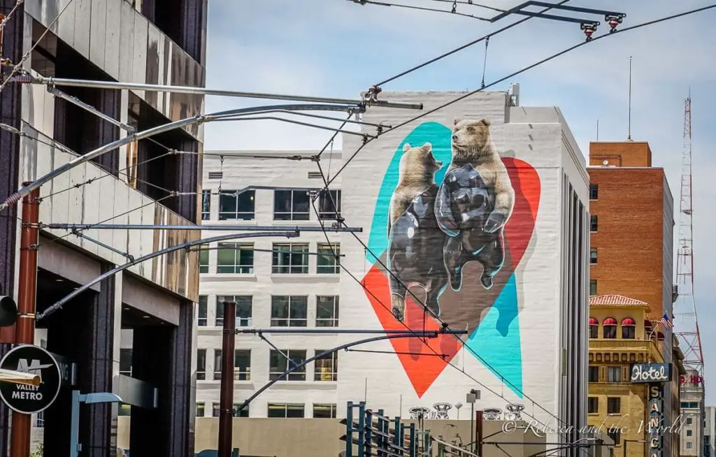 A large mural on a building featuring two bears standing against a backdrop of a heart, with a blue sky behind them. There are so many great murals to see on a weekend in Phoenix.