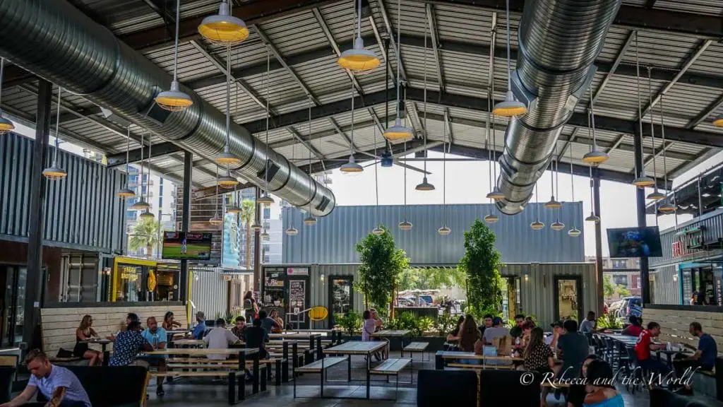 An indoor dining area with an industrial ceiling, pendant lights, and a mix of patrons seated at wooden tables, enjoying their meals. The Churchill in Phoenix AZ is a fun place for a drink or bite to eat.