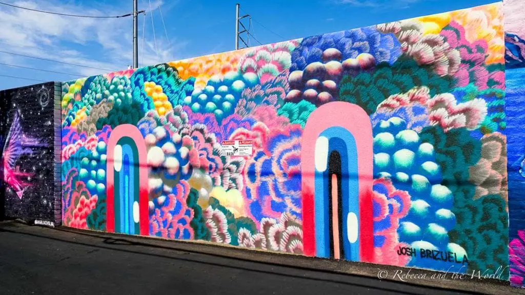 A colorful mural covering a long wall, with cloud-like patterns in vibrant hues and two abstract door shapes in the center. Make sure you include street art on your Phoenix itinerary.