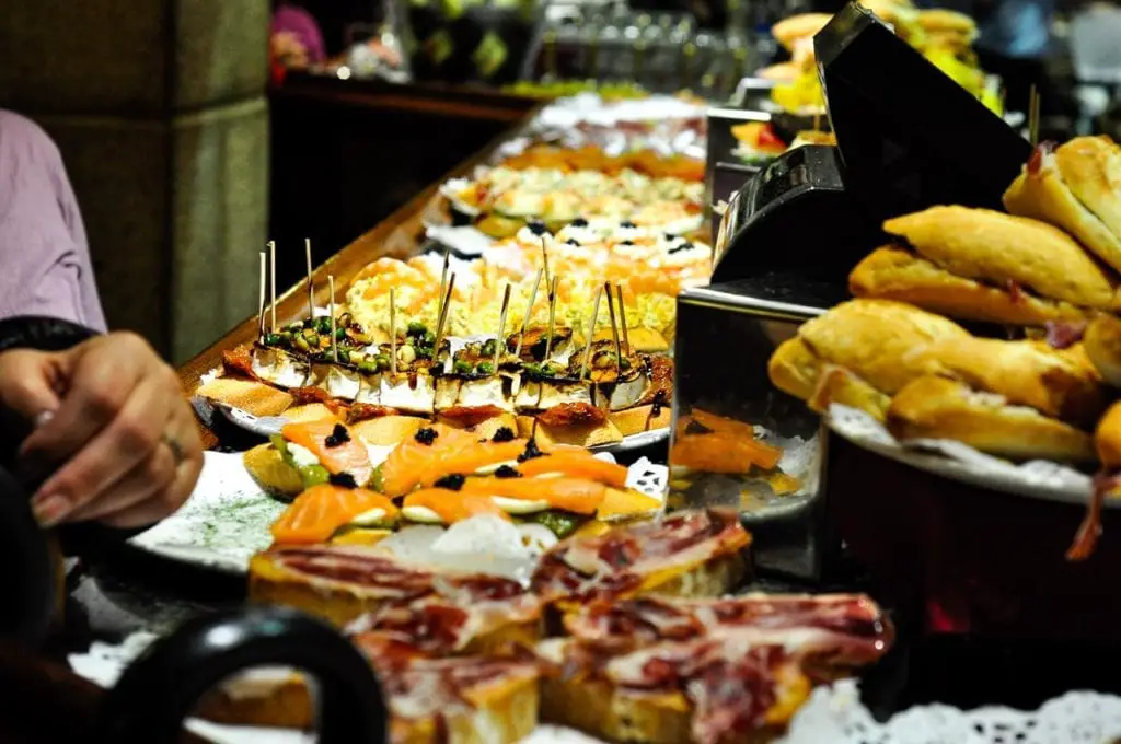 A close-up of an array of traditional Basque pintxos, including slices of baguette topped with various ingredients like salmon, cheese, and Iberico ham, all neatly arranged and garnished, ready for consumption. Undoubtedly one of the best things to do in San Sebastian is to try local pintxos, bite-sized morsels of delicious food.