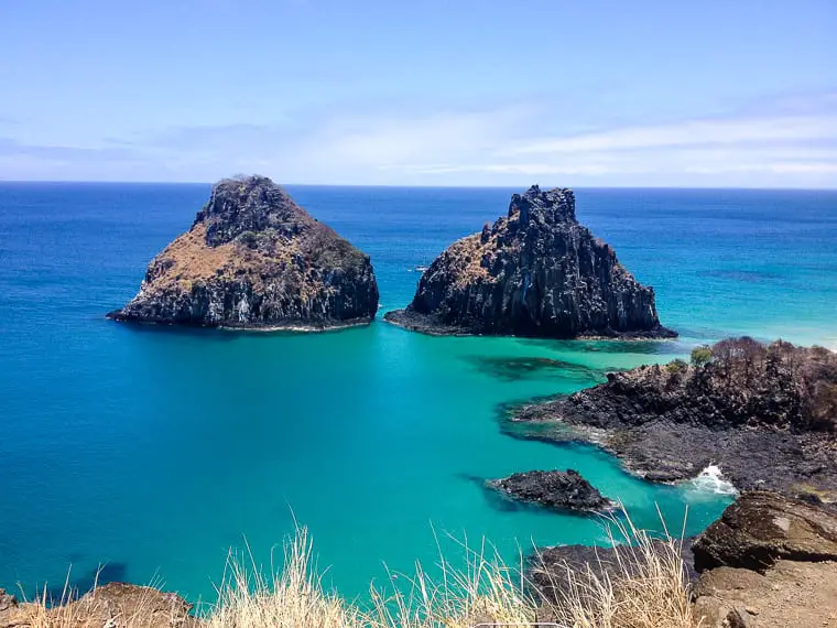 Two dramatic, rocky islets rising from a turquoise sea, viewed from a high vantage point along the coast of Fernando de Noronha, Brazil. Without a doubt one of the most beautiful places to visit in Brazil is Fernando de Noronha, a UNESCO Heritage Site whose sensitive environment is carefully protected.