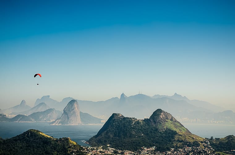 A paraglider soars above lush green mountains with Rio de Janeiro’s iconic Sugarloaf Mountain and city skyline in the background, under a clear blue sky. Every Brazil itinerary will include a trip to Rio de Janeiro at one point or another. This city is so full of energy, it's one of the essential places to visit in Brazil.