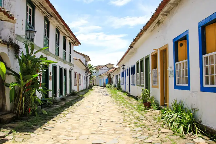 Charming colonial street in Paraty, lined with white buildings featuring brightly painted doors and windows, and a stone paved road. A colourful, colonial town in Brazil, Paraty is one of the most fun places to visit in Brazil!