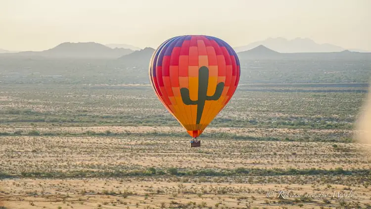 A colourful hot air balloon with a cactus on it floats over the desert outside of Scottsdale, Arizona