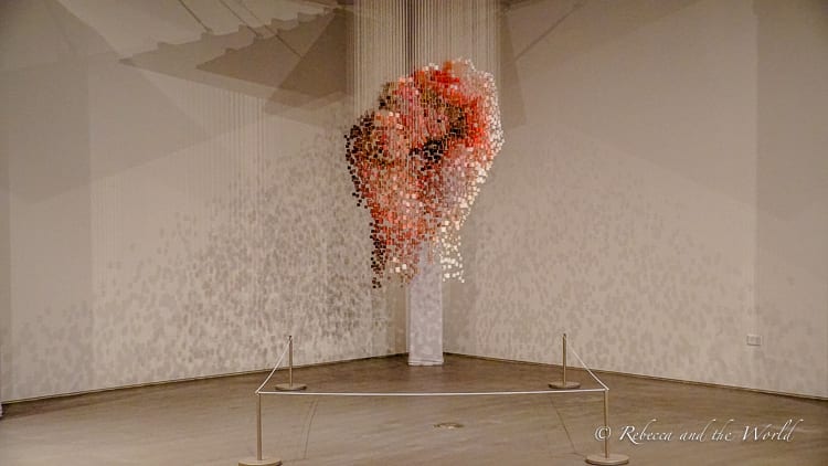 An art installation of a heart made from suspended red and clear crystals creating a floating, three-dimensional shape, displayed in a gallery with controlled lighting to accentuate its form.