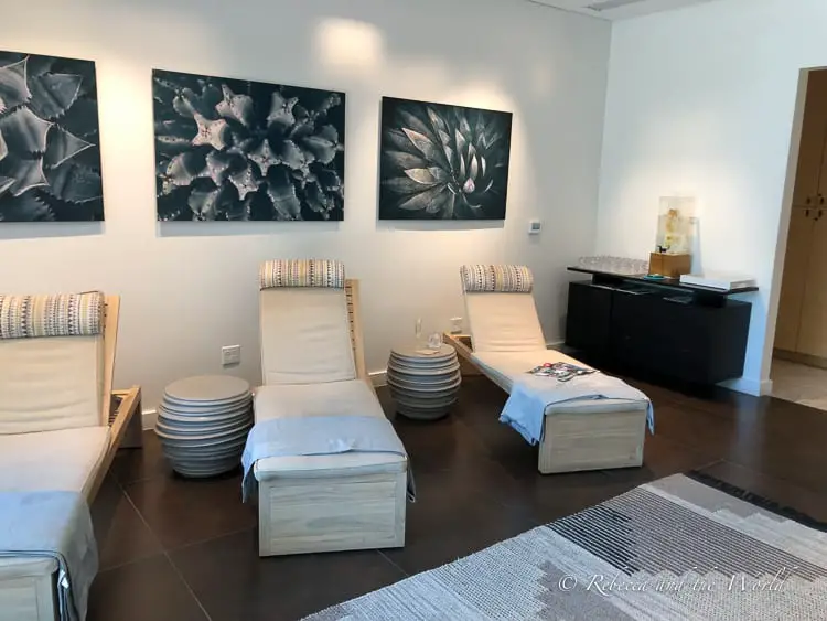 A tranquil spa lounge room with neutral tones, displaying wall art of agave plants, comfortable reclining chairs, and neatly stacked towels, inviting relaxation. Scottsdale has more than 50 spas!