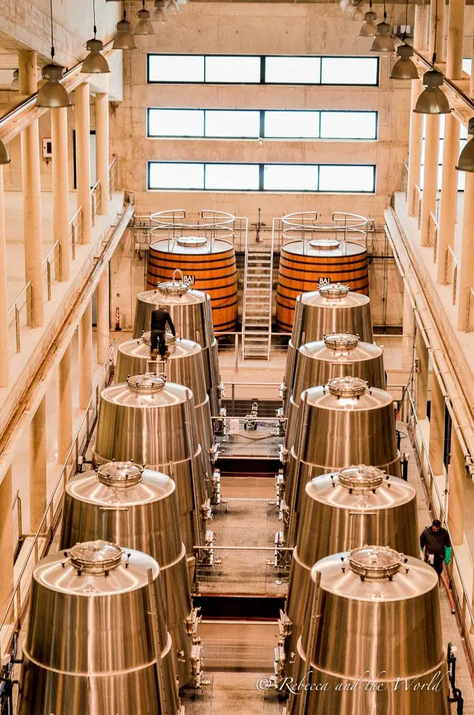 Interior of a modern winery in La Rioja, with stainless steel fermentation tanks lined up symmetrically and a central walkway leading to the end of the facility. Bodegas Baigorri is one of the most modern wineries in La Rioja.