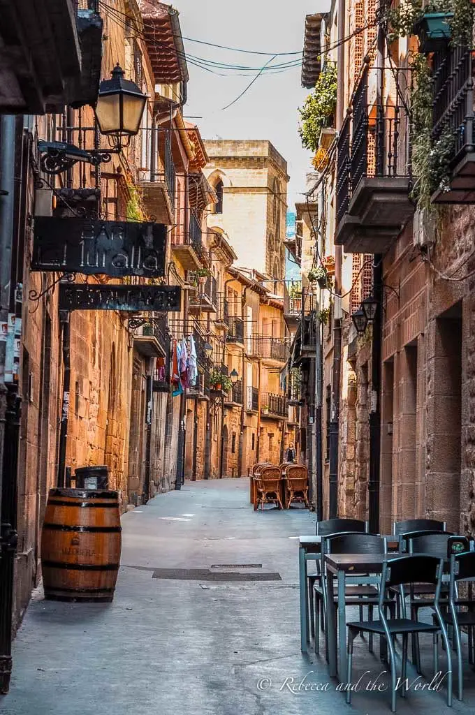 A charming street in a village in the La Rioja region with stone buildings, hanging lanterns, and a wine barrel sign, evoking the ambiance of the region's small towns. There are many gorgeous villages sprinkled throughout La Rioja wine region.