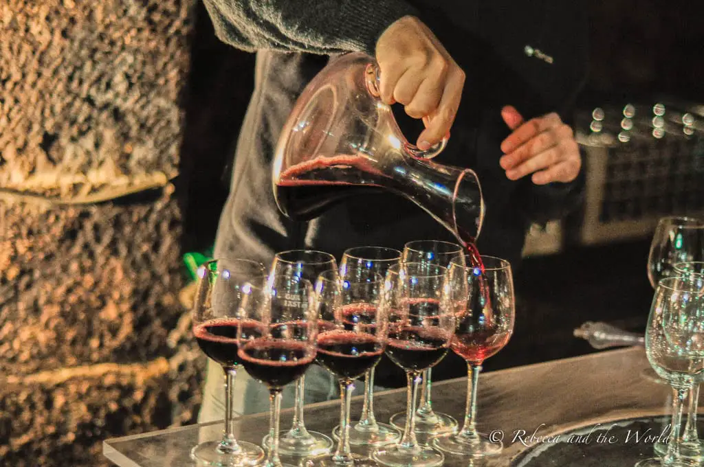 A hand pouring red wine from a decanter into a row of glasses, capturing the wine-tasting experiences offered throughout La Rioja. There are plenty of old wineries throughout La Rioja.