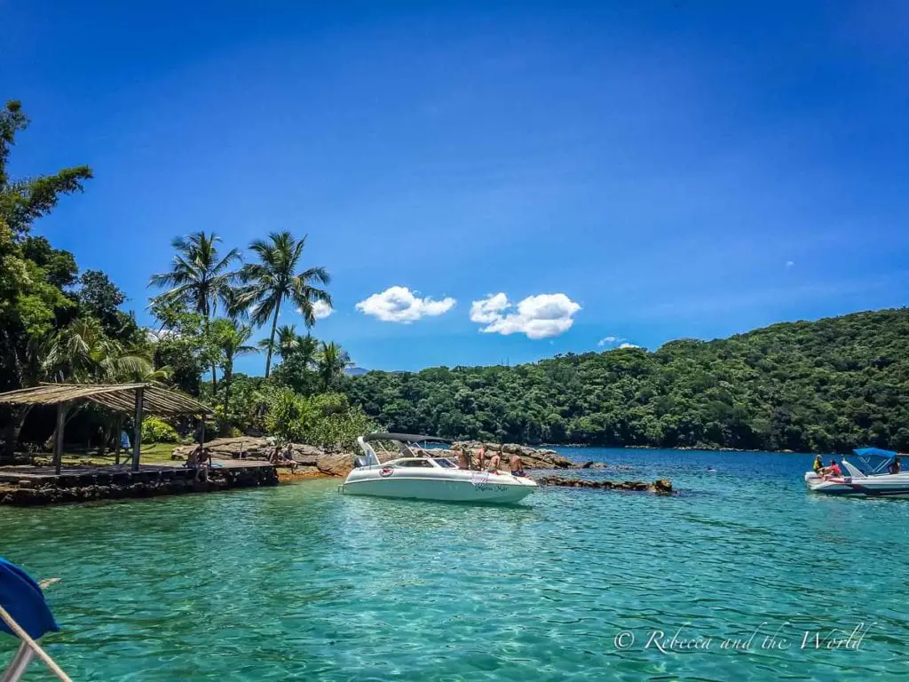 Peaceful seaside scene on Ilha Grande with boats moored near a lush coastline under a clear blue sky. Wondering what to do in Ilha Grande? Join a beach tour to explore some of Brazil's best beaches.