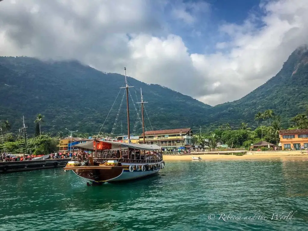 Traditional boat filled with tourists docking at a vibrant waterfront on Ilha Grande, with people and colourful buildings along the shore. Boats arriving at the main dock in Ilha Grande.