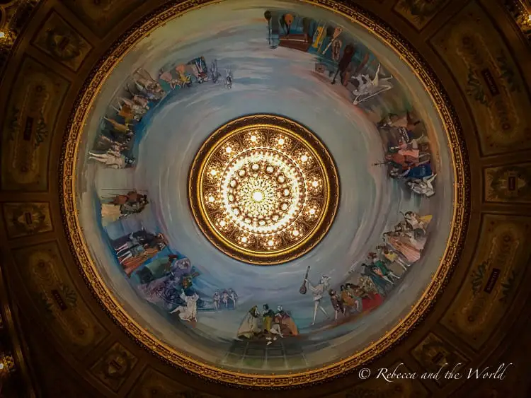 The ornate ceiling fresco and grand chandelier of Teatro Colón, Buenos Aires' main opera house, showcasing the luxurious interior design. The Teatro Colon is one of the most beautiful buildings and things to see in Buenos Aires.