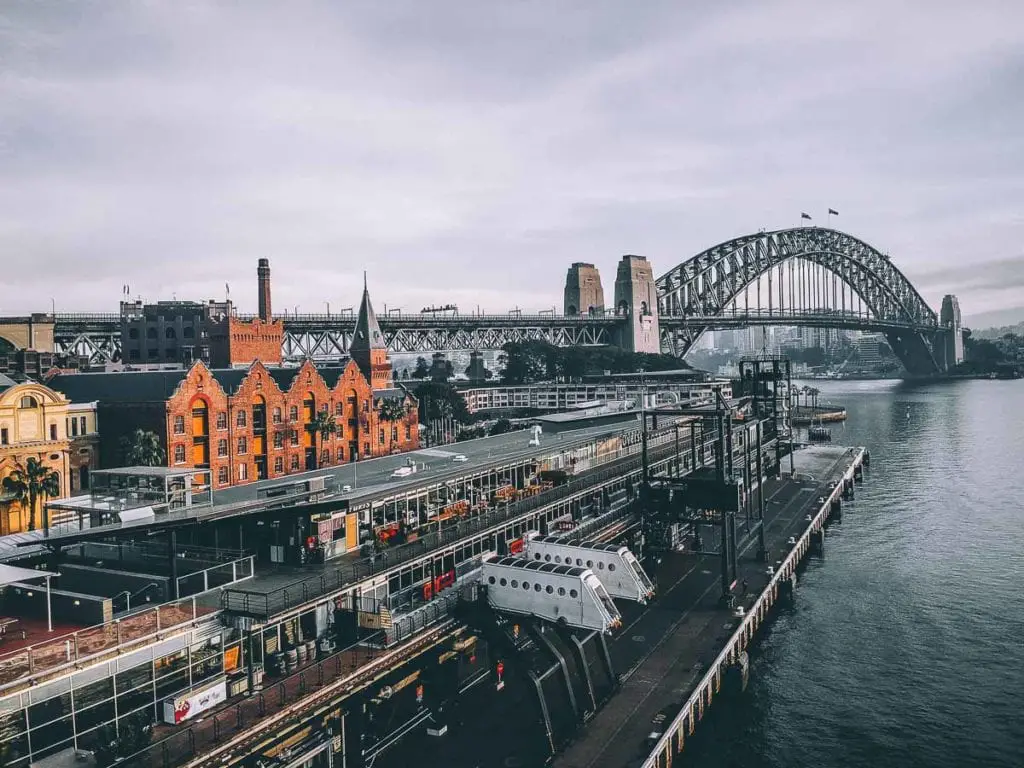 Historic The Rocks and Sydney Harbour Bridge view, with a quaint red-brick building in the foreground. The Sydney Harbour Bridge is an iconic image of Sydney. You can walk it, bike it, drive a car across it or even climb to the top!