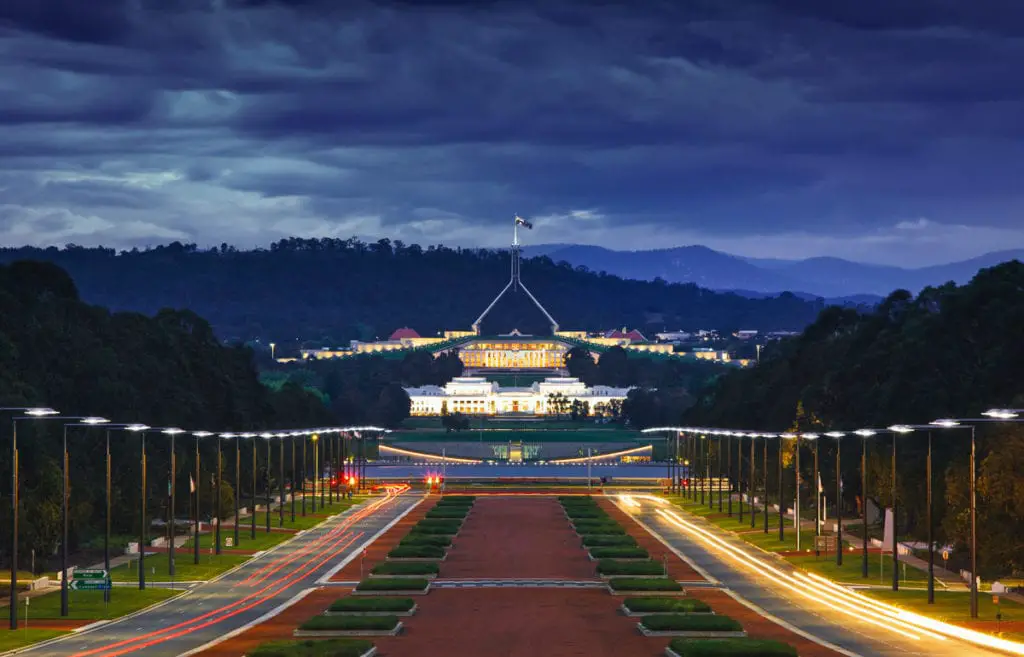 View of the Australian Parliament House in Canberra at dusk, with illuminated roadways leading to the grand building and dark clouds overhead. Canberra, the capital city of Australia, is now one of the most up-and-coming places to visit in Australia with plenty of history, hip cafes and restaurants.
