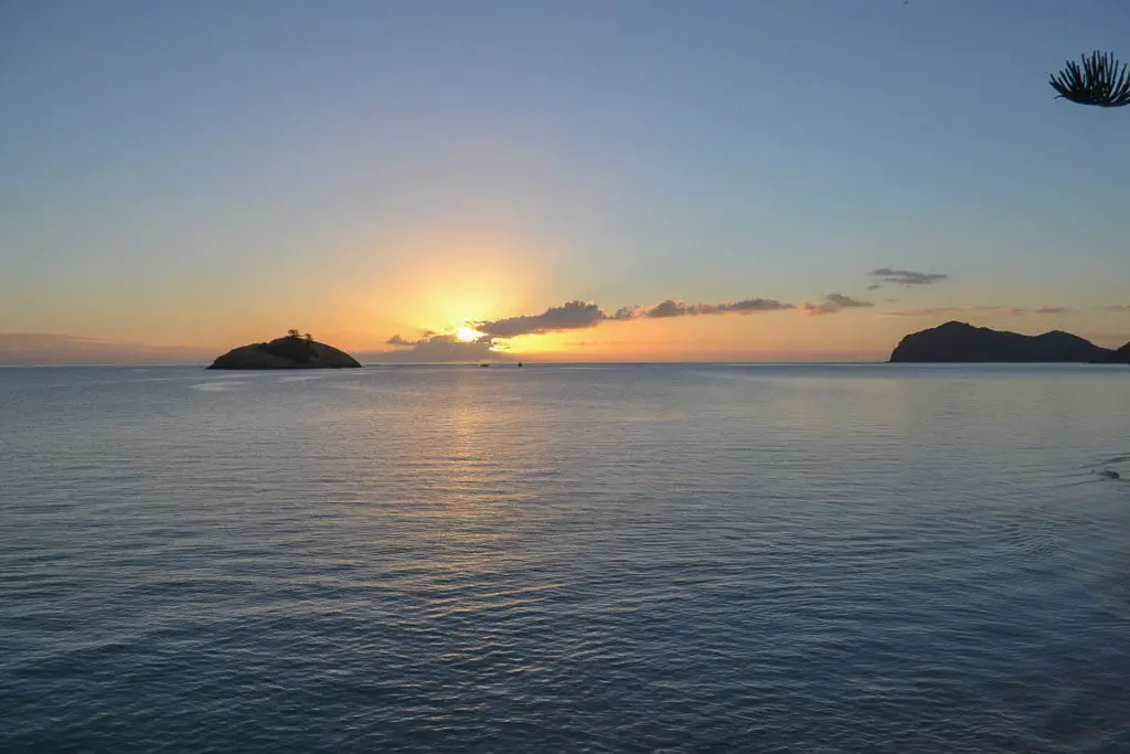 Sunrise view from a tranquil bay looking out to a small island, with the sun peeking over the horizon. Only 400 people are allowed to stay on Lord Howe Island in Australia at any one time.