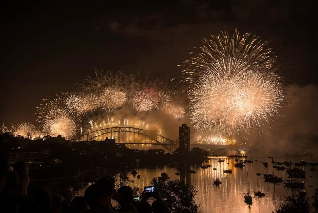 Fireworks display illuminating Sydney Harbour Bridge, with spectators in silhouette watching the spectacle. If you're looking for a huge New Year's Eve party look no further than Sydney. It's one of the first cities in the world to ring in the new year.