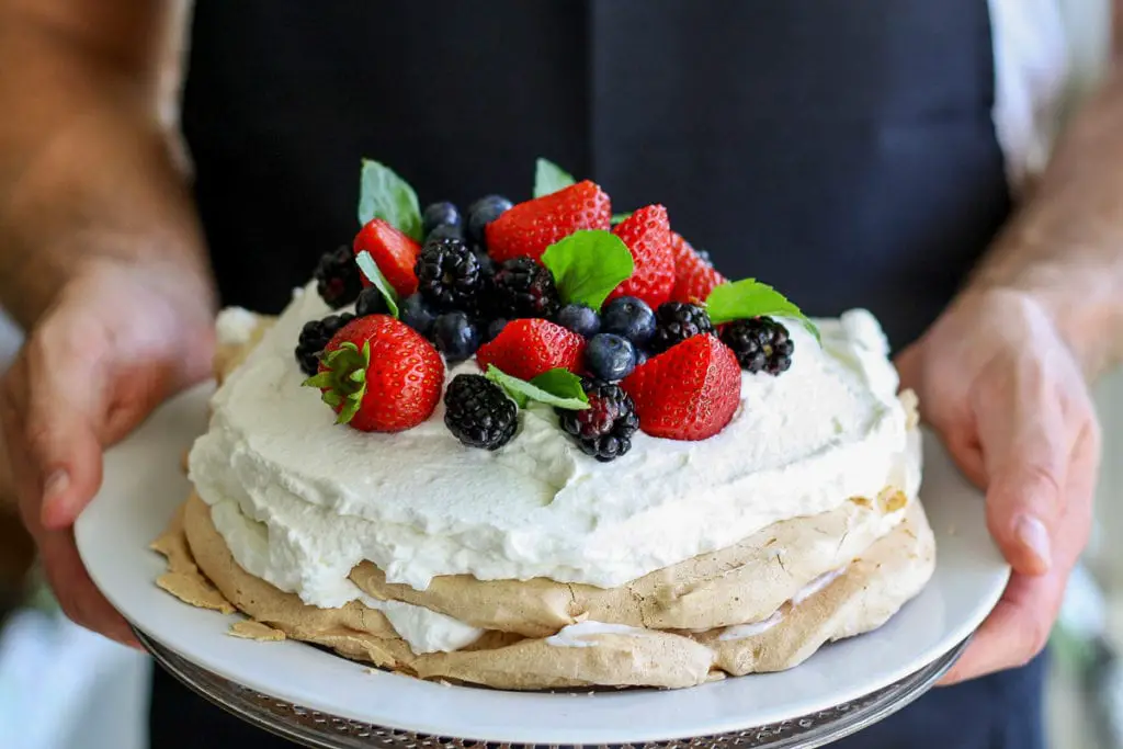 A close-up of a traditional Australian pavlova dessert adorned with fresh strawberries, blueberries, and blackberries on top of whipped cream. Pavlova is a delicious dessert you can eat in Australia (although New Zealanders will claim that they created it first).