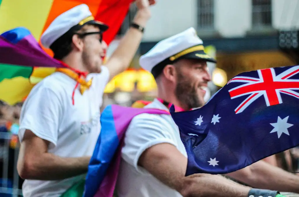 Two individuals wrapped in an Australian flag and pride flags, celebrating at an outdoor event. Mardi Gras is one of the biggest parties in Sydney, Australia.