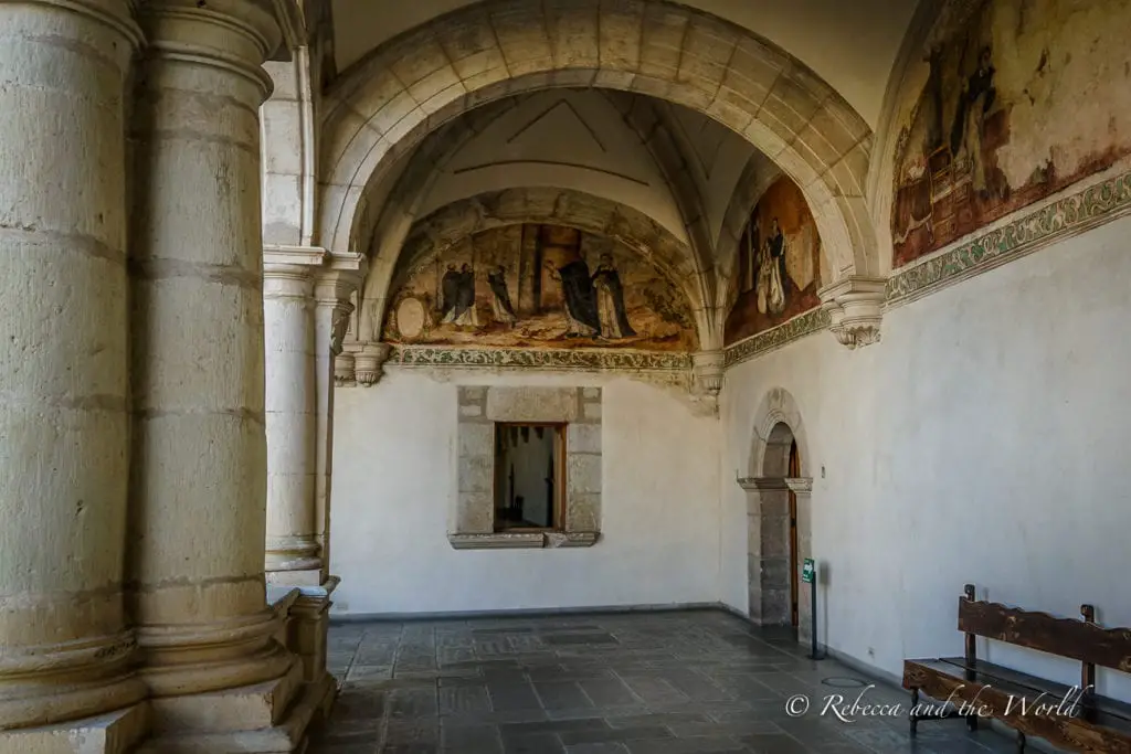 An arched corridor with weathered walls adorned with faded frescoes. The corridor is part of a historic building with stone columns and a patterned floor, leading to a bright doorway. Plan to spend a few hours of your Oaxaca itinerary exploring the interesting Oaxaca Culture Museum.