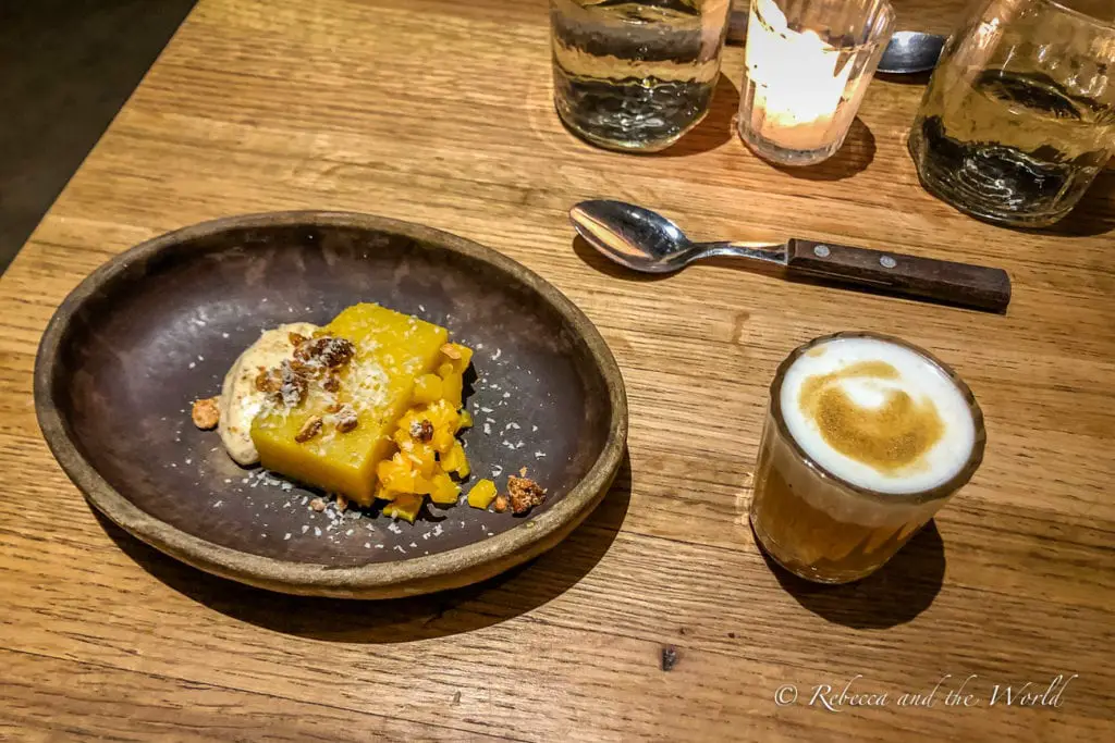 A rustic dessert presentation on a wooden table. Beside the plate is a spoon and a small glass of espresso with a layer of foam on top. The food at Criollo is to-die-for - make sure you book a reservation at this restaurant as you plan your Oaxaca itinerary