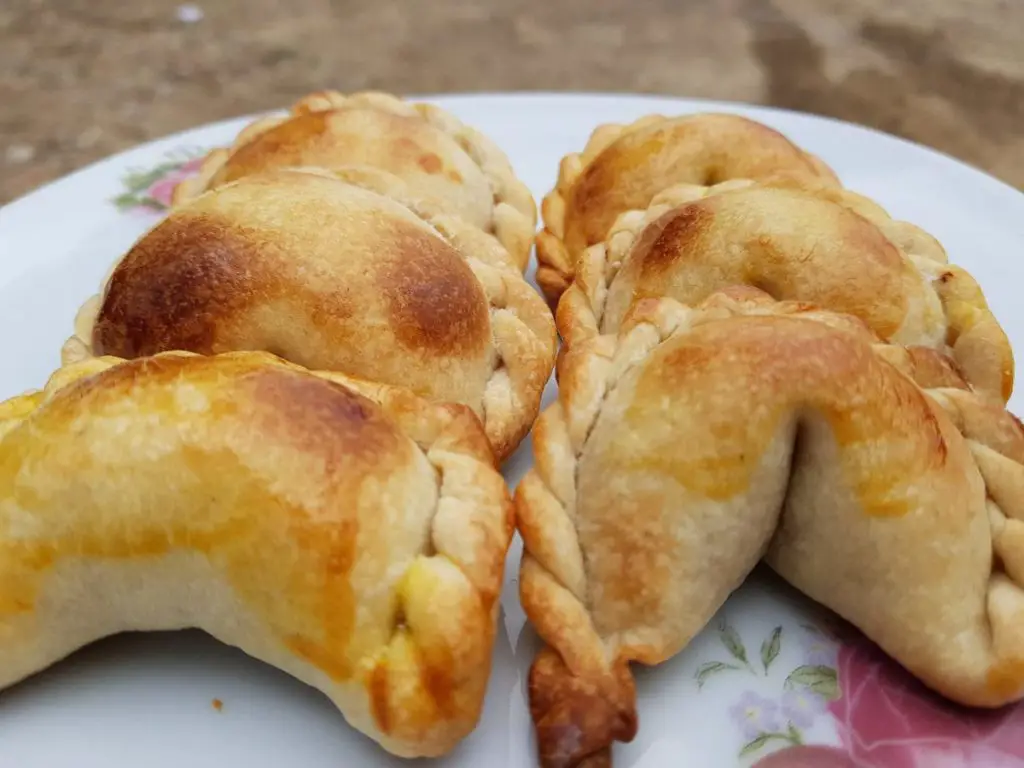 A close-up of a plate with several golden-brown empanadas with crimped edges, suggesting they are baked. Empanadas are a great snack if you're wondering what to eat in Buenos Aires.