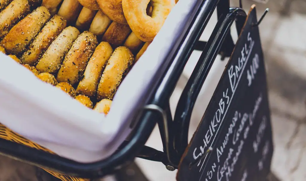 A basket filled with various seasoned bagels, next to a blackboard sign with handwritten menu items. Sheikob's Bagels is one of the best casual restaurants in Buenos Aires.