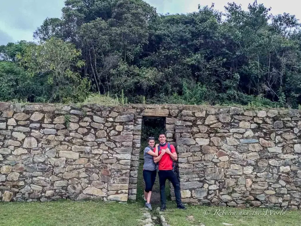 Two hikers - the author and her husband - posing in front of an ancient stone structure with a doorway, surrounded by dense forest on the Salkantay Trek.