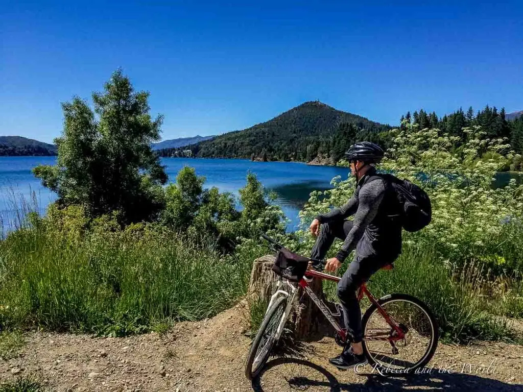 A man in black sits on a stationary bike overlooking a blue lake on the Circuito Chico route in Bariloche, Argentina. 