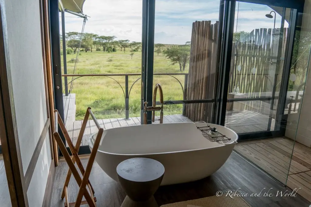 An elegant freestanding bathtub in a room with large windows offering a view of the savanna outside. The tents at Lemala Nanyukie in Tanzania are pure luxury.