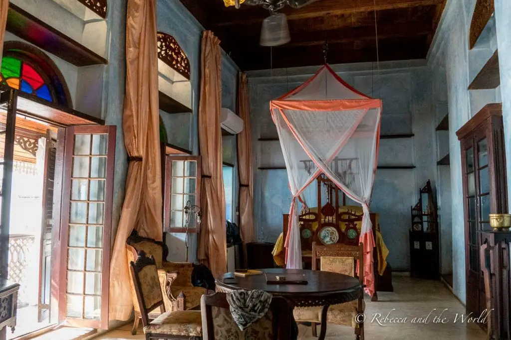 An interior view of a room with antique furniture, draped curtains, and a four-poster bed with a mosquito net. The Emerson Spice Hotel is one of the best places to stay in Stone Town in Zanzibar.