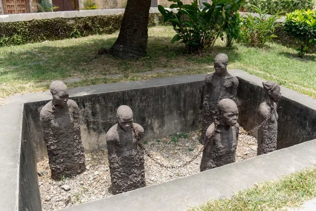 Sculptures of chained individuals standing in a sunken pit, representing the historic plight of slaves. One of the best things to do in Stone Town in Zanzibar is a walking tour of the city.