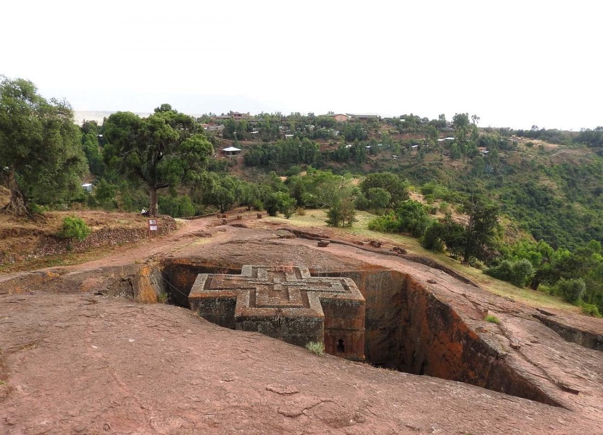 The rock-hewn church of Saint George in Lalibela, Ethiopia, an architectural marvel carved from a single piece of rock in the shape of a cross, with surrounding trees and distant hills in view. Ethiopia is one of the many countries I'd love to visit.