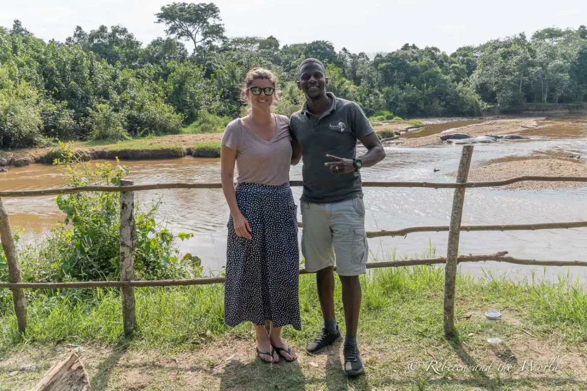 A man and a woman - the author of this article and her private guide in Uganda - standing beside a river in a lush green setting, smiling towards the camera. There are so many tour operators in Uganda, and I recommend Ellington Safaris.