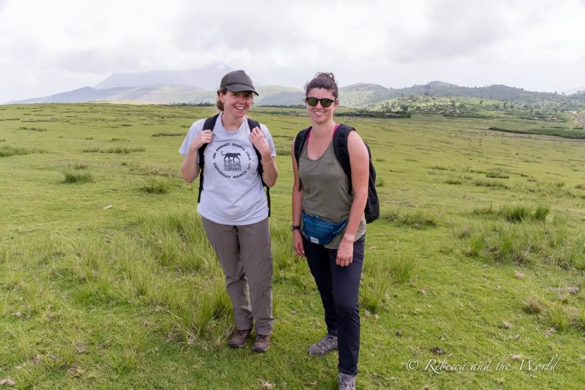 Two women - one the author of this article - standing on a grassy plain with distant hills, smiling at the camera, illustrating the type of scenery experienced on foot during a guided safari. There are many safari companies in Tanzania, but I recommend Safari Republic.