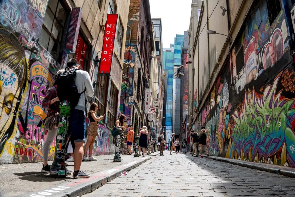 Vibrant street art covering the walls of an urban alley in Melbourne, Australia, with people walking and taking photos. This is Hosier Lane, one of Melbourne's most famous street art laneways.