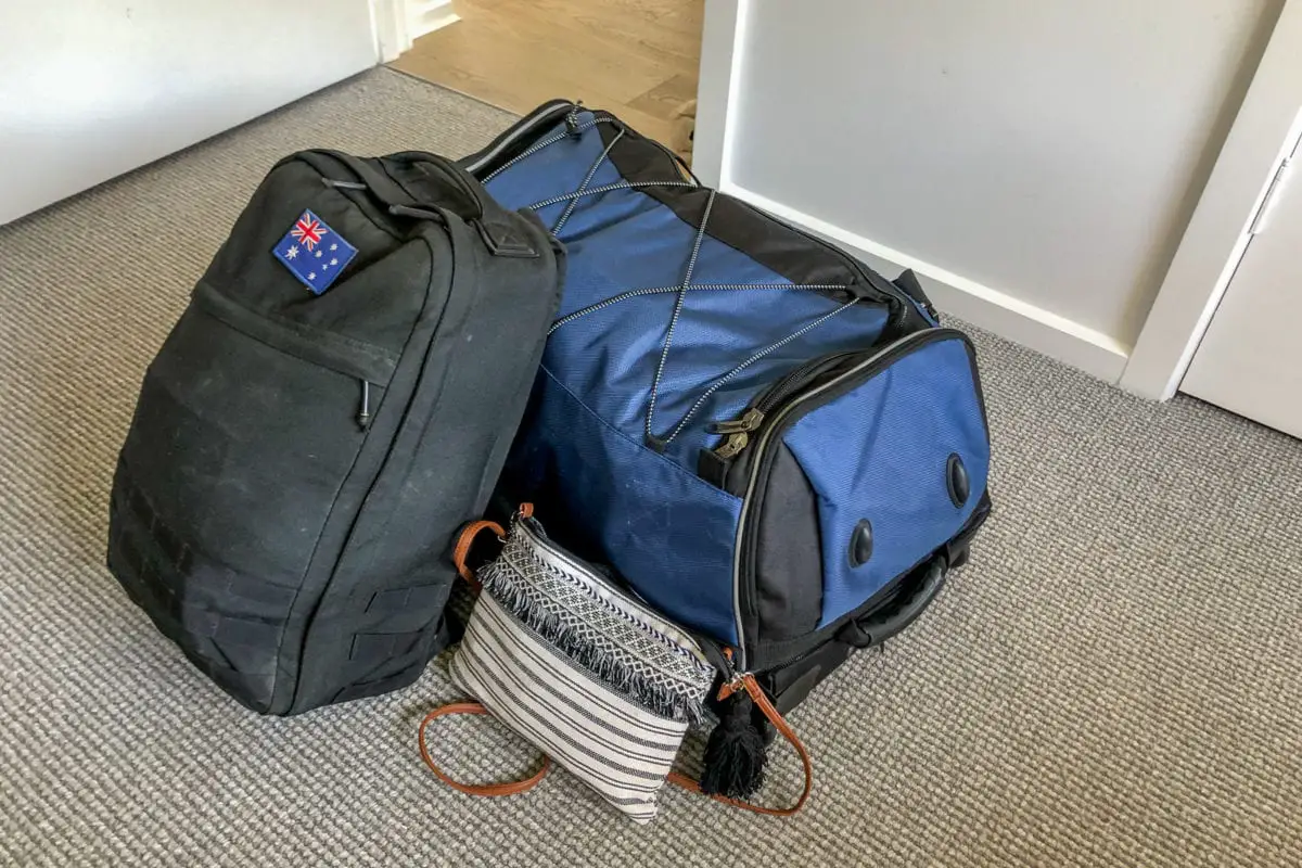 Everything on this East Africa packing list fits into these three bags! Photo shows a black backpack with an Australian flag on it, a large blue and black bag and a small black and white handbag - all bags are filled with clothing and items for the trip to East Africa.