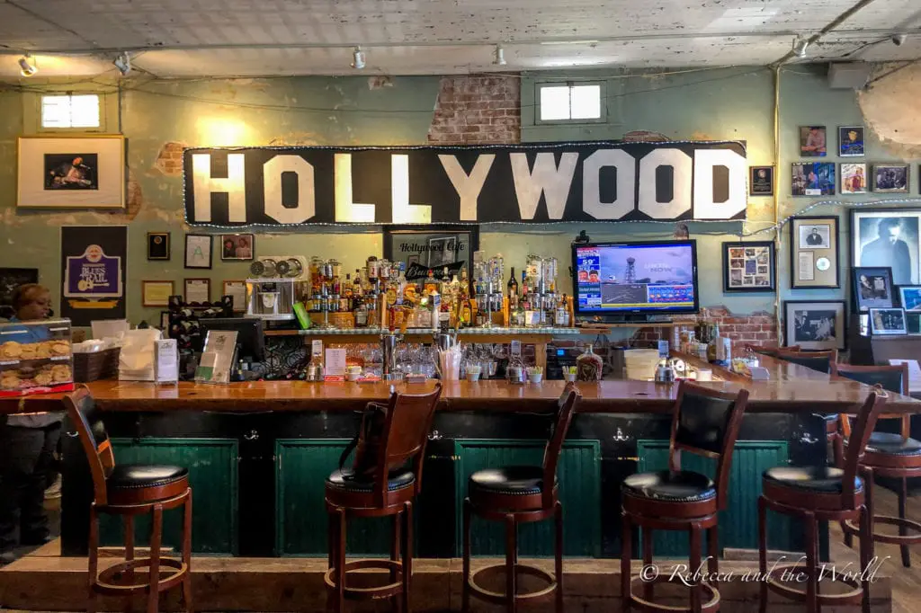 Inside a bar named Hollywood, with a vintage feel, wooden bar stools, and walls adorned with framed photos and a large illuminated 'HOLLYWOOD' sign. Hollywood Cafe in Tunica, MS.