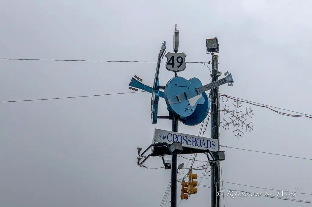 A unique guitar-shaped signpost for 'The Crossroads' at the intersection of Highway 49, against a cloudy sky, representing the legendary crossroads of blues folklore. The Crossroads in Clarksdale, MS where Robert Johnson allegedly sold his soul to the devil.