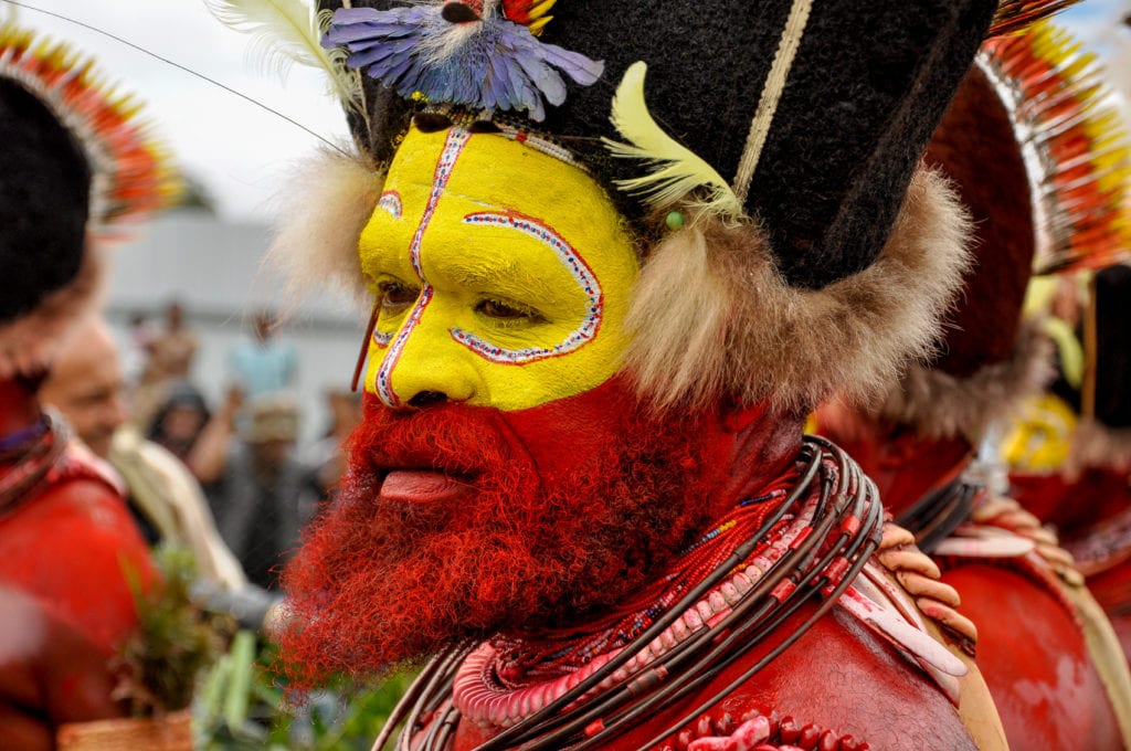 A Huli Wigman with face painted yellow and red, adorned with colorful beads and feathers, participating in a cultural ceremony called a sing sing. The Highlands of Papua New Guinea are a fascinating - although challenging - place to visit.