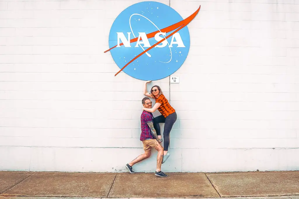 Two people posing playfully in front of a large NASA logo on a wall, evoking a sense of fun and adventure in space exploration. Huntsville, Alabama, is one of the most fun cities to visit in the USA - visit the space centre to learn how to be an astronaut!