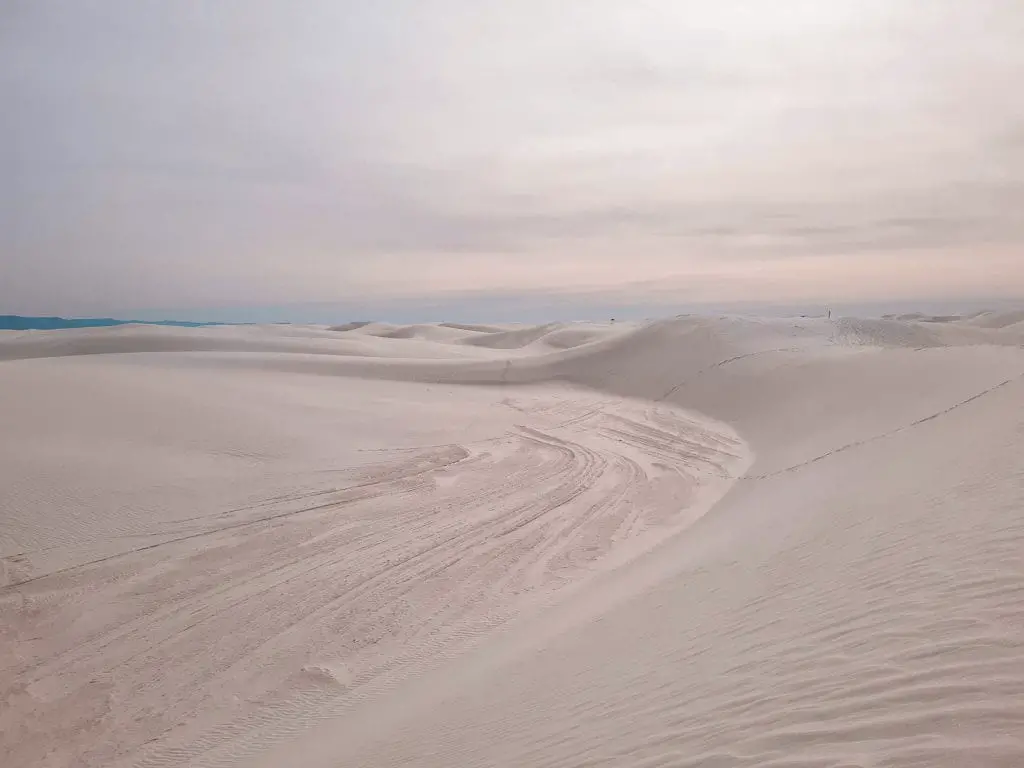 Expansive white sand dunes stretching into the distance under a pale sky at White Sands National Park, New Mexico, creating a peaceful, otherworldly landscape. White Sands National Park is one of the more unique places to visit in the US - here you can go sand boarding on the dunes!
