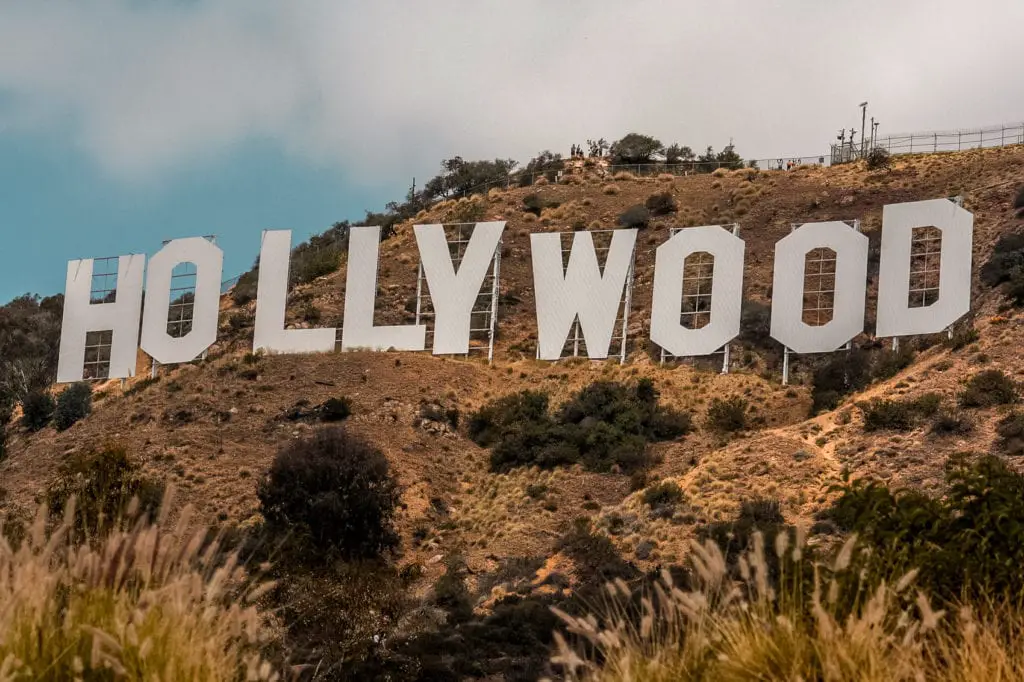 The famous Hollywood sign on a hillside, with the letters clearly visible and a brush-filled foreground under a cloudy sky. Los Angeles is one of the most fun cities to visit in the US - but traffic is bad!