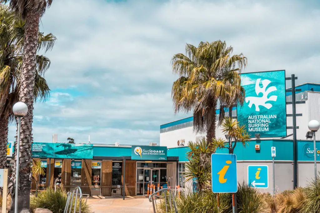 Facade of the Australian National Surfing Museum with visitor information signs and palm trees in the foreground. The Australian National Surfing Museum is in Torquay and provides a great history of surfing.