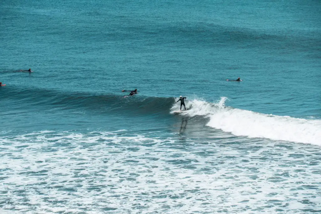 Surfers riding waves in the ocean at Bells Beach, Victoria, with one standing on a surfboard on a wave, and others paddling nearby. One of the coolest things to do along the Great Ocean Road is to see surfers in action!