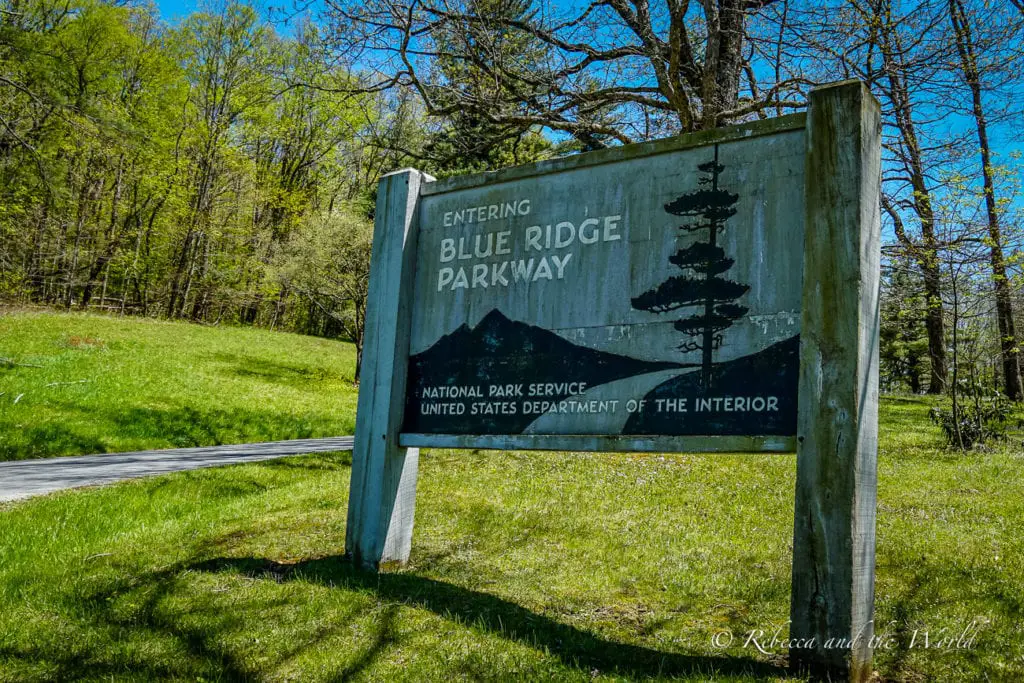 A wooden sign indicating the entrance to the Blue Ridge Parkway, with the National Park Service emblem, surrounded by a lush green landscape.