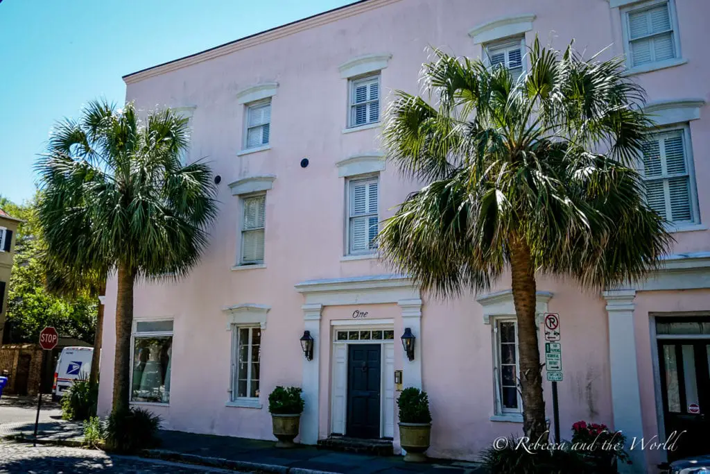 A row of colorful buildings with palm trees in front, creating a picturesque street scene. The buildings are painted in pastel pink, blue, and green, with traditional shutters on the windows.