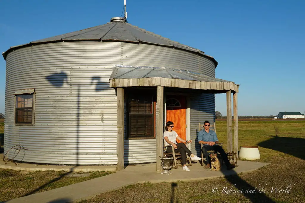 A corrugated metal grain silo converted into a dwelling, with two people - the author and her husband - and a dog sitting on chairs outside, enjoying the expansive flat farmland surrounding them. Stay at the Shack Up Inn in Clarksdale Mississippi for unique accommodation like this former grain shed.