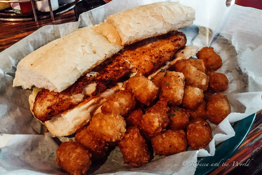 A close-up of a po'boy sandwich with fried shrimp on a crusty baguette, served with a side of golden-brown hush puppies, presented on a paper-lined tray.