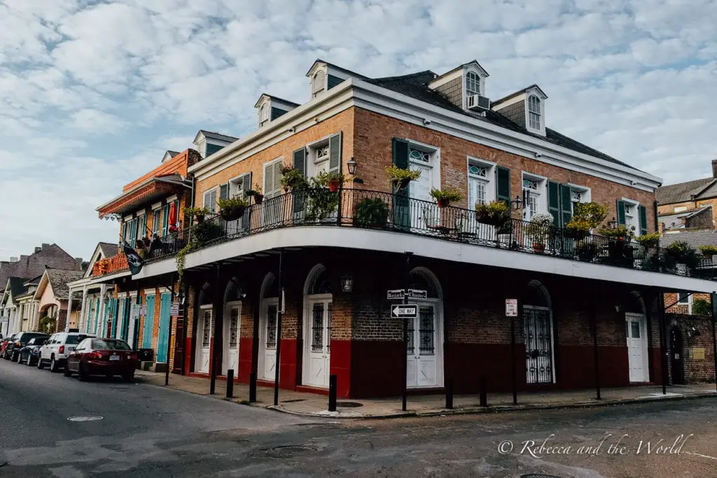 A street corner in a historic district with two-story buildings displaying a mix of French and Spanish architectural styles, with wrought-iron balconies and colourful shutters. New Orleans is a must-stop destination on a Deep South road trip.