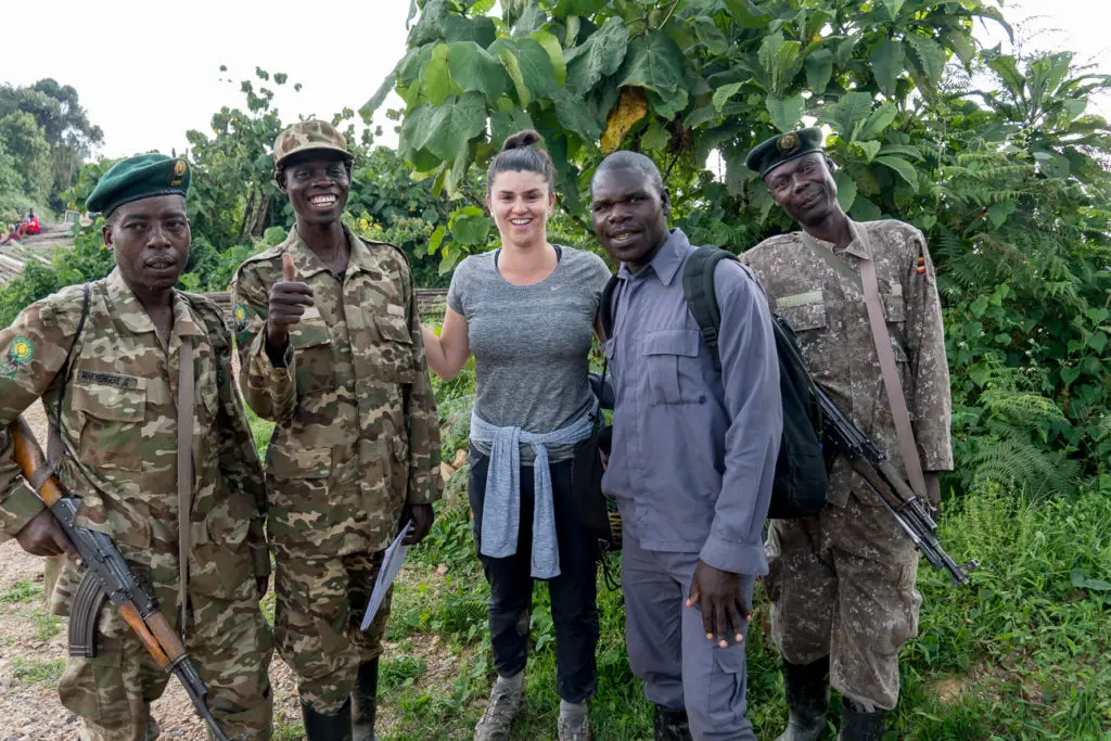 Four individuals in camouflage military uniforms, some carrying rifles, posing for a photo with a smiling woman - the author of this article - in casual clothing. They are standing in a lush, green area.